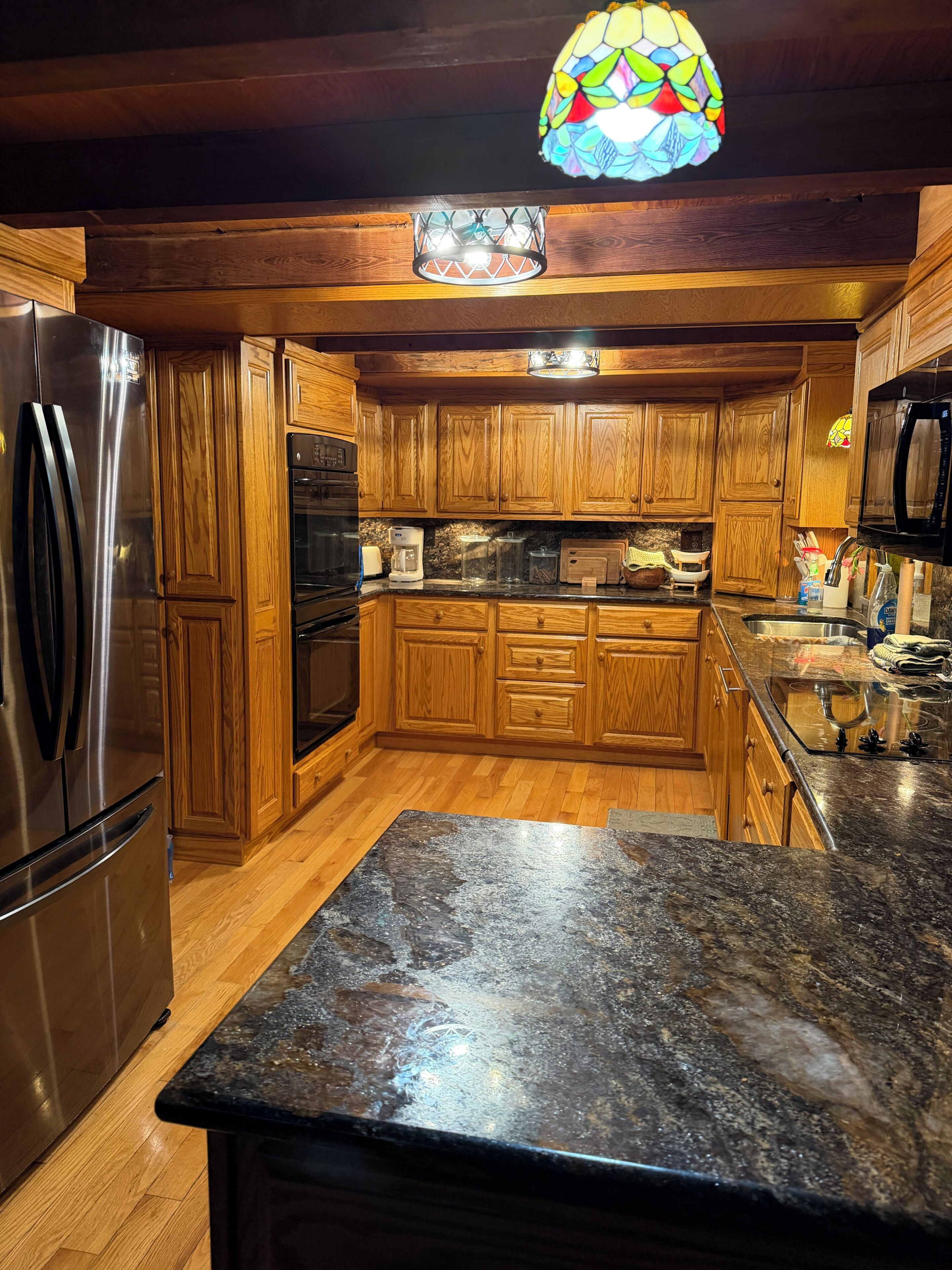 A kitchen with wooden cabinets, stainless steel appliances, a granite countertop, and a stained glass light fixture.