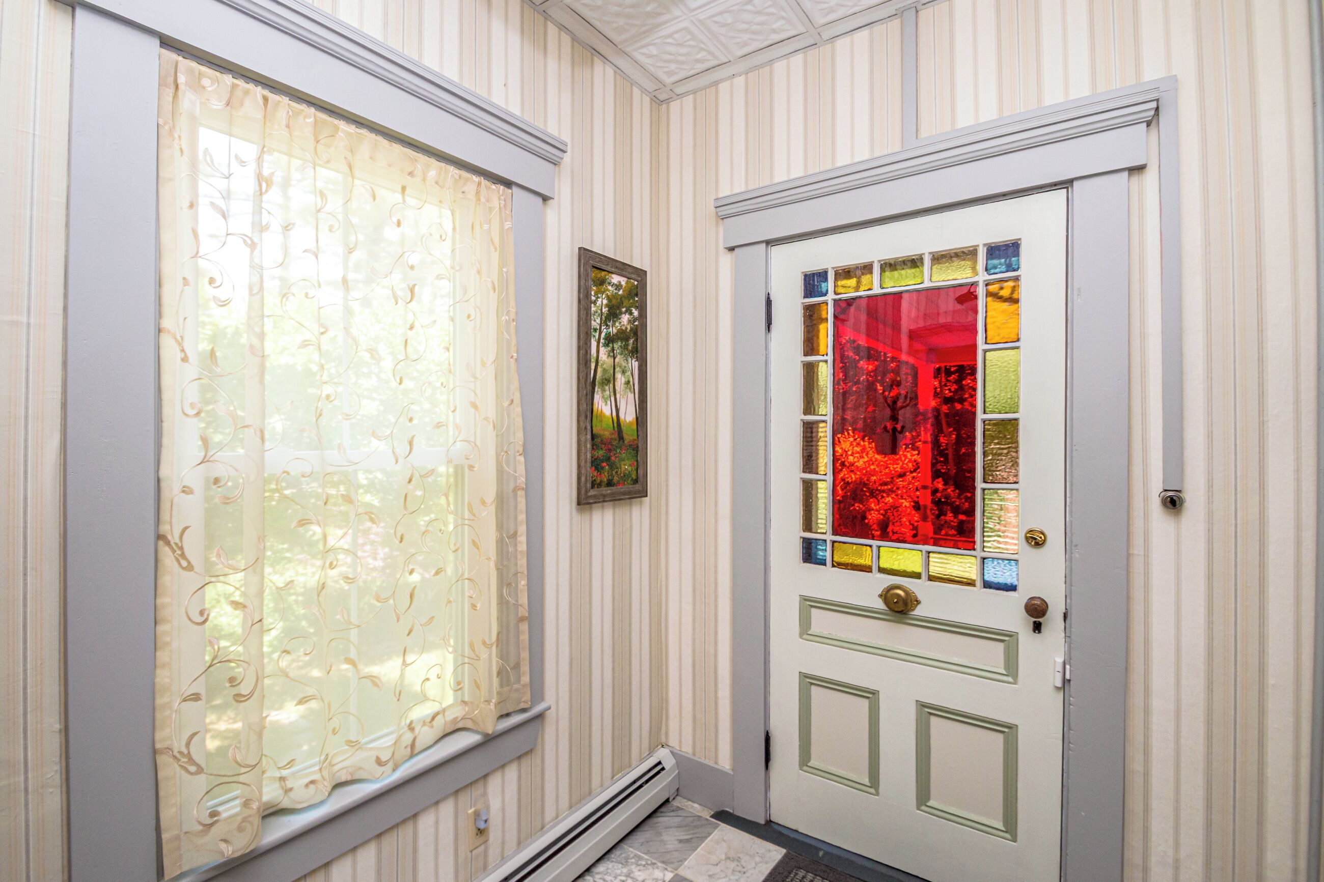 A hallway with a door featuring a stained glass design and a window with a sheer curtain.
