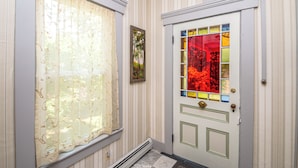 A hallway with a door featuring a stained glass design and a window with a sheer curtain.