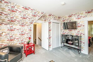 A room with a patterned wallpaper, a television, a red side table, and a black leather chair. - RoseWood Landing (Silver Lake)