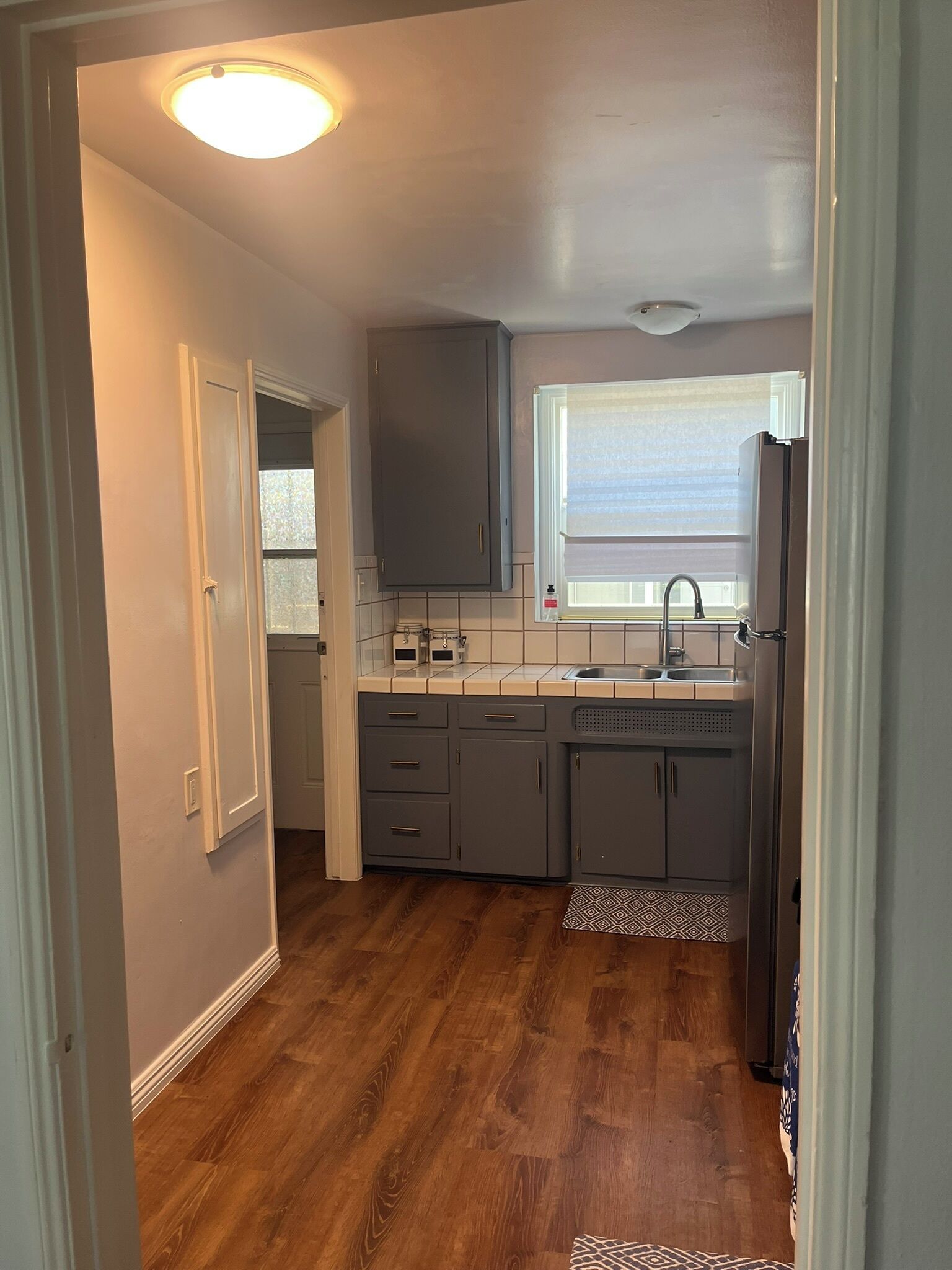 A kitchen with grey cabinets, a window with blinds, and a wooden floor.