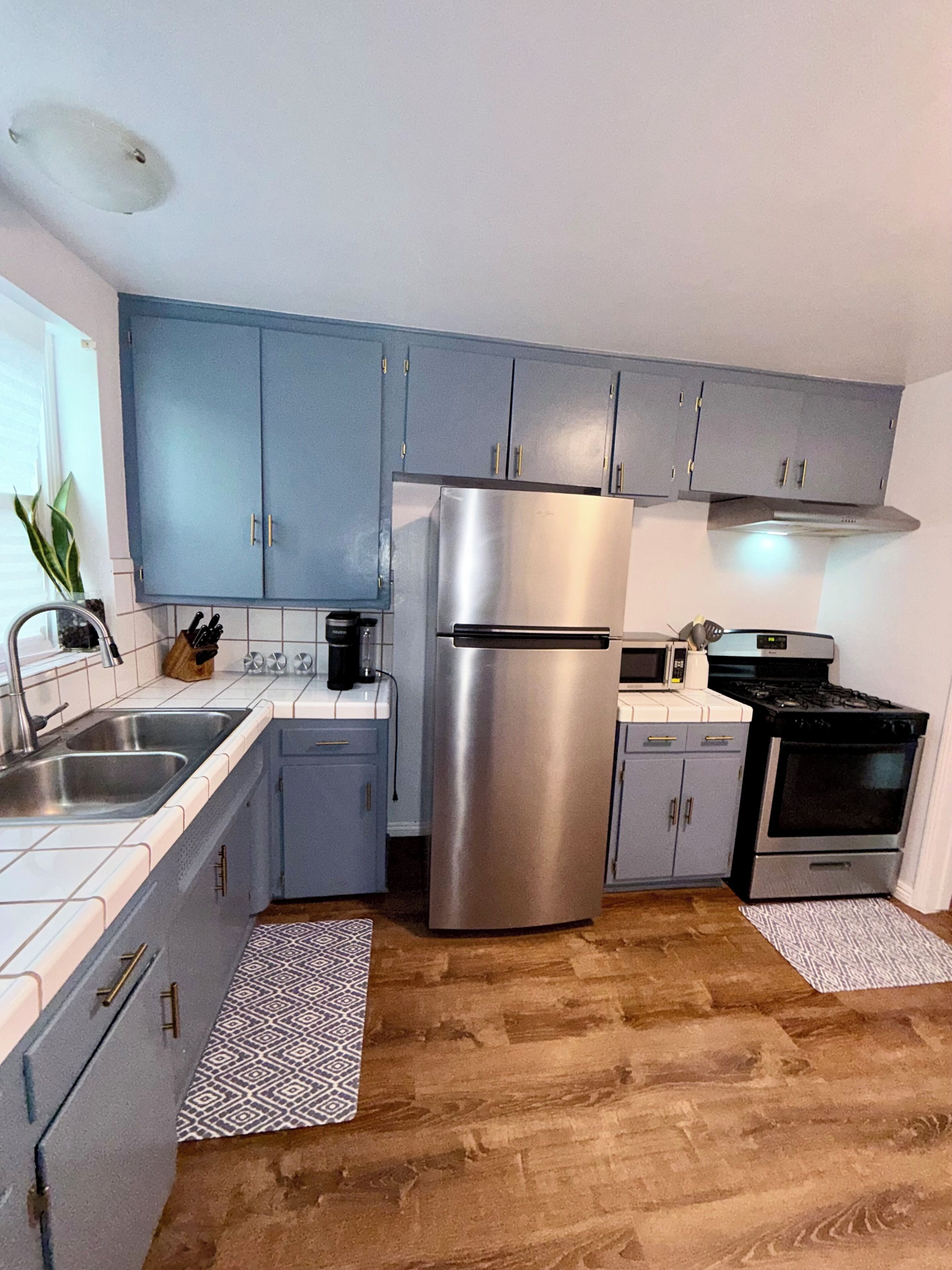 A kitchen with grey cabinets, stainless steel appliances, a sink, and a patterned rug.