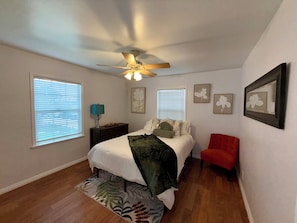Un dormitorio con cama, una silla roja, ventilador de techo y decoración en la pared.