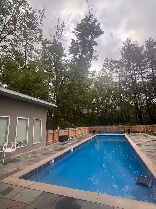 A rectangular swimming pool with a tiled edge, surrounded by a wooden fence and trees.