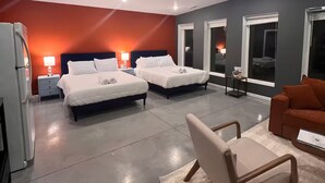 Quarto de hotel moderno com duas camas, um sofá, uma mesinha e um refrigerador.