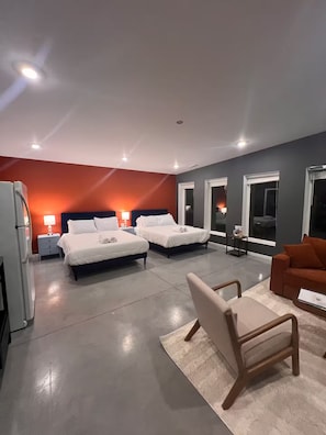 A modern hotel room with two beds, a sofa, a small table, and a refrigerator.