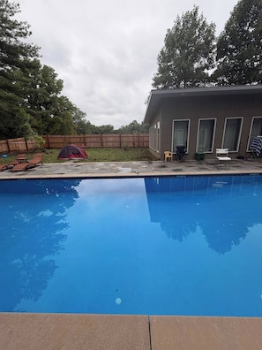 A swimming pool with a wooden deck and lounge chairs.
