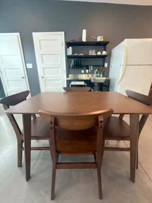 A dining area with a wooden table and chairs, a kitchen area with cabinets and appliances, and a door.