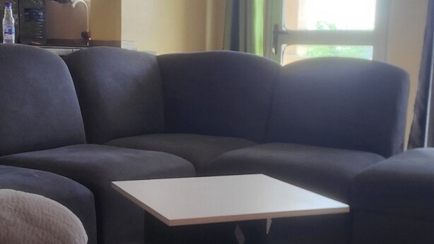 Ein Wohnzimmer mit einem dunkelgrauen Sofa, einem kleinen Tisch und einem Fenster mit Vorhängen.