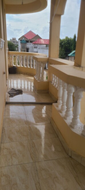 A balcony with a tiled floor and white balustrades, overlooking a building with a red roof. - Adorable 1-bedroom building in Kwale County perfect for relaxing stay (Kwale County)