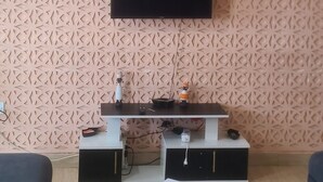 Ein Wohnzimmer mit flachbildfernseher an einer Wand mit Muster, einem Deckenventilator und einem kleinen Tisch mit TV-Stand.