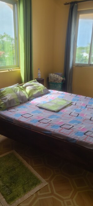 A room with a bed, a small table, a water bottle, and a window with curtains. - Adorable 1-bedroom building in Kwale County perfect for relaxing stay (Kwale County)