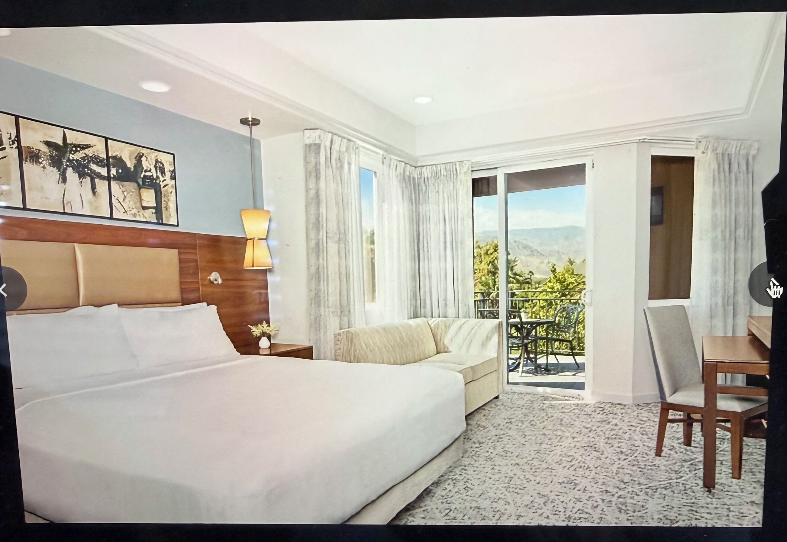 Une chambre d’hôtel avec un lit, un canapé, un bureau et un balcon offrant une vue.