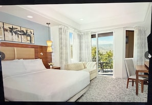 A hotel room with a bed, a sofa, a desk, and a balcony with a view.