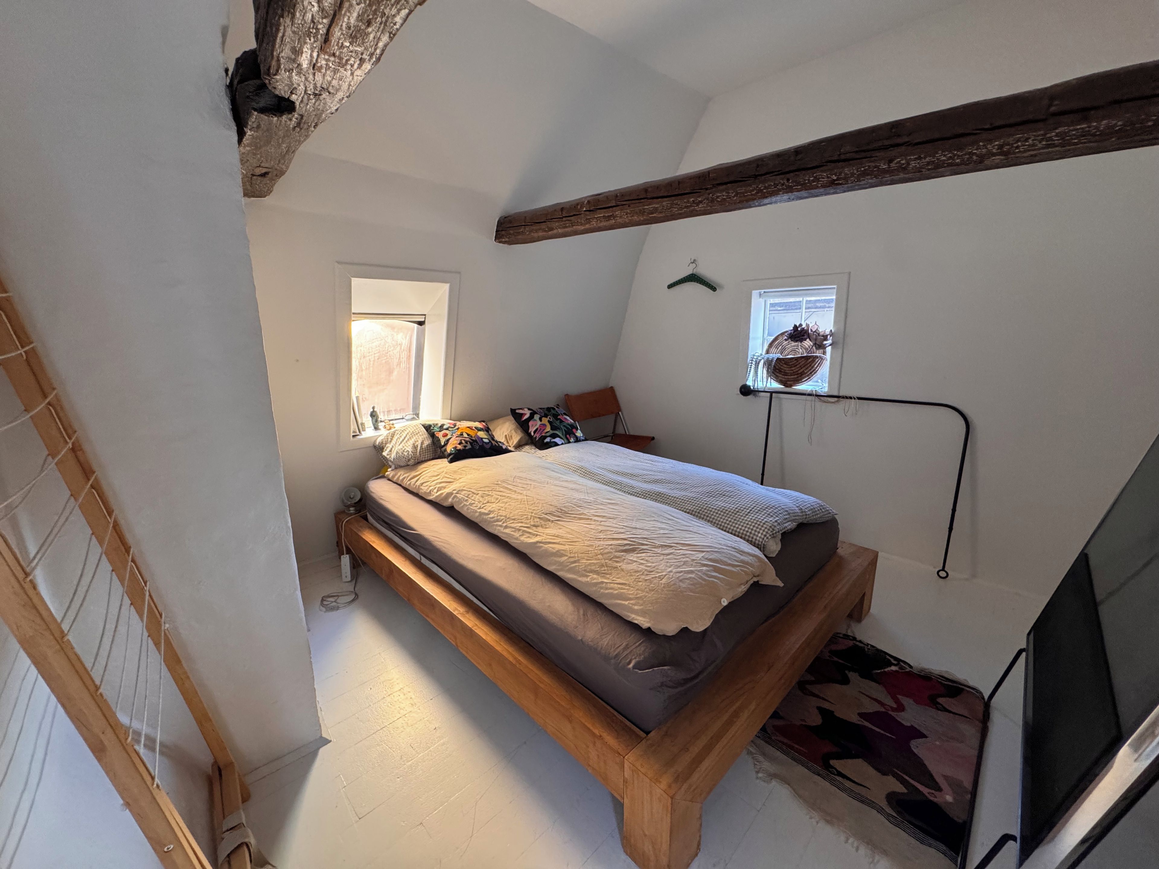 A bedroom with a wooden bed, a window, a hanging basket, and a TV stand.