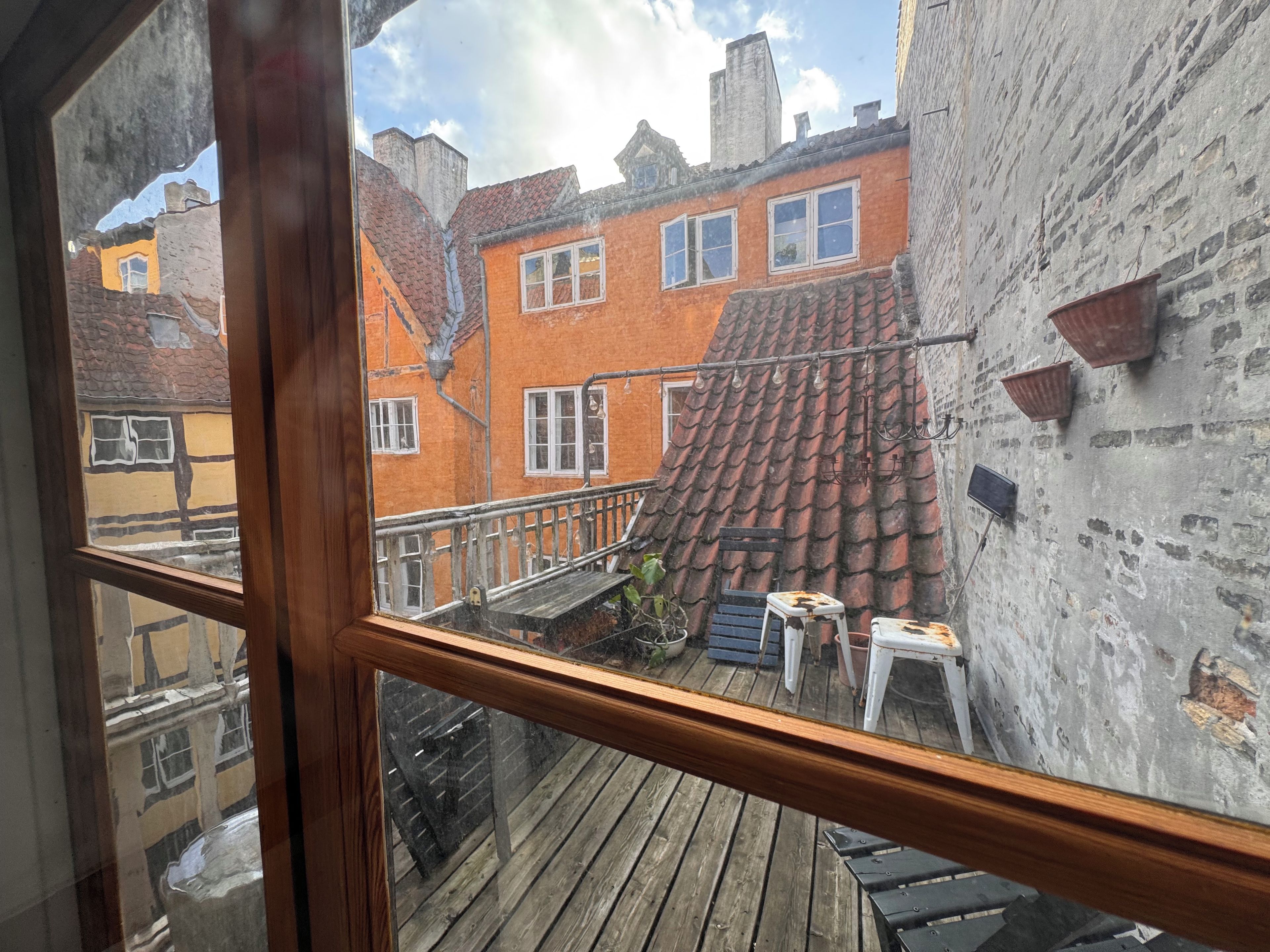 Un balcon en bois offrant une vue sur un immeuble en briques, doté de nombreuses fenêtres et d’un toit recouvert de tuiles.