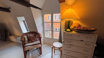 A cozy room with a wooden chair, a white dresser, a lamp, and a view of a building through a window.