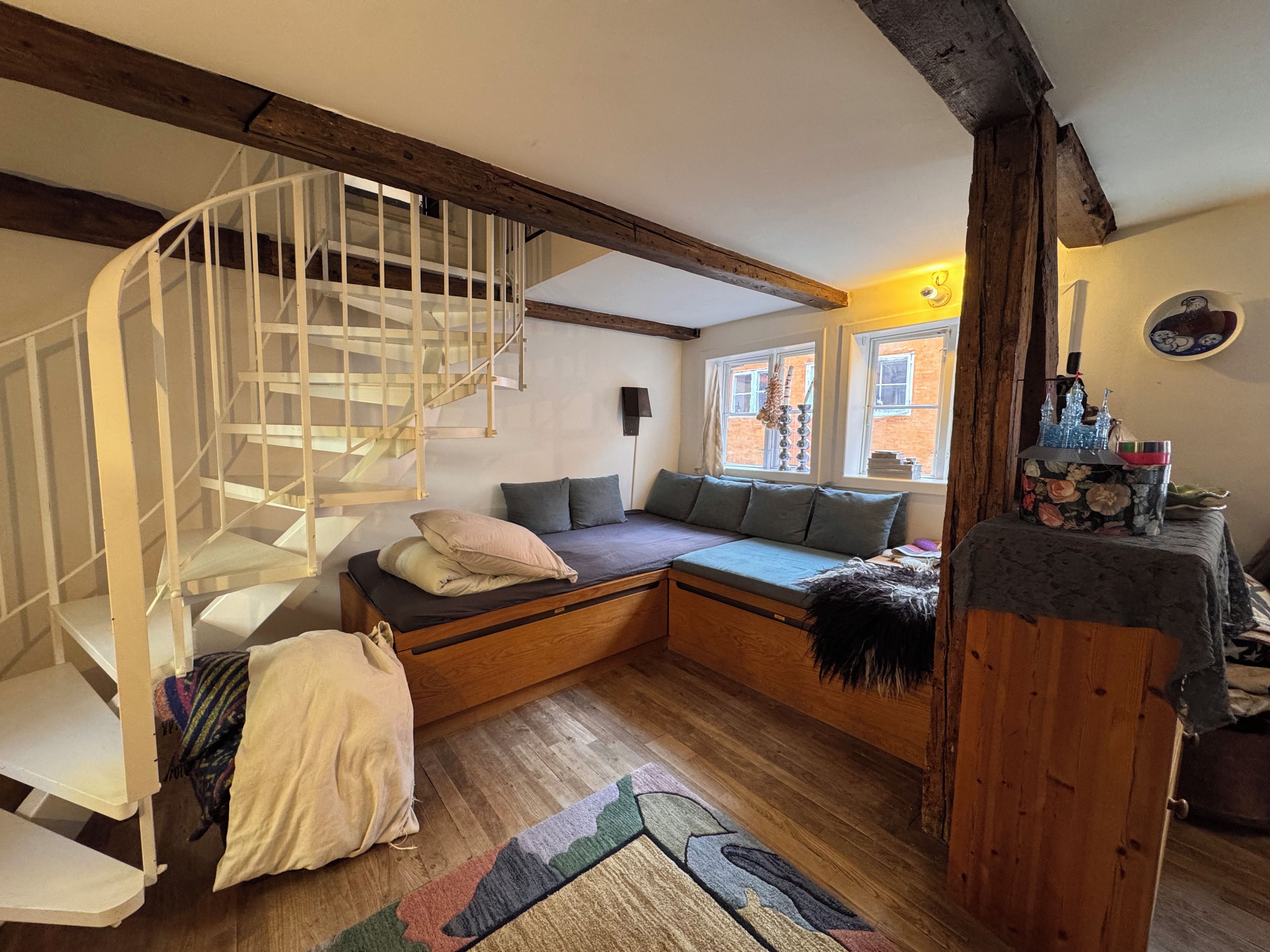 Una stanza con una scala a chiocciola, un divano letto, pavimento in legno e una finestra vista esterna.