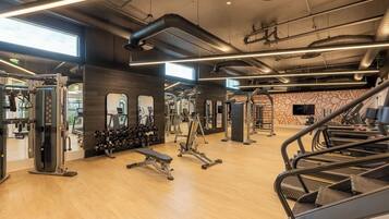 A gym with various exercise equipment, wooden flooring, and large windows allowing natural light.