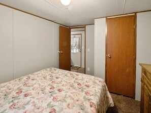A bedroom with a floral bedspread, a wooden door, and a dresser. - 2-bedroom mobile home with a sleeping sofa in peaceful Mammoth Cave with AC. (Mammoth Cave)
