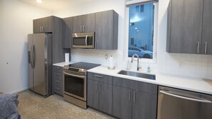 A modern kitchen with stainless steel appliances, grey cabinetry, a window with a view of a car, and a tiled backsplash. - New Townhouse in Historic District of Chattanooga (Chattanooga)