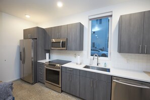 A modern kitchen with stainless steel appliances, grey cabinetry, a window with a view of a car, and a tiled backsplash. - New Townhouse in Historic District of Chattanooga (Chattanooga)