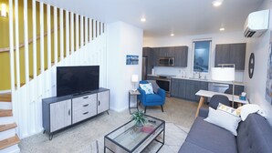 A modern living space with a flat-screen TV, sofa, coffee table, and a staircase with wooden railings. - New Townhouse in Historic District of Chattanooga (Chattanooga)