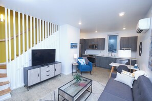 A modern living space with a flat-screen TV, sofa, coffee table, and a staircase with wooden railings. - New Townhouse in Historic District of Chattanooga (Chattanooga)
