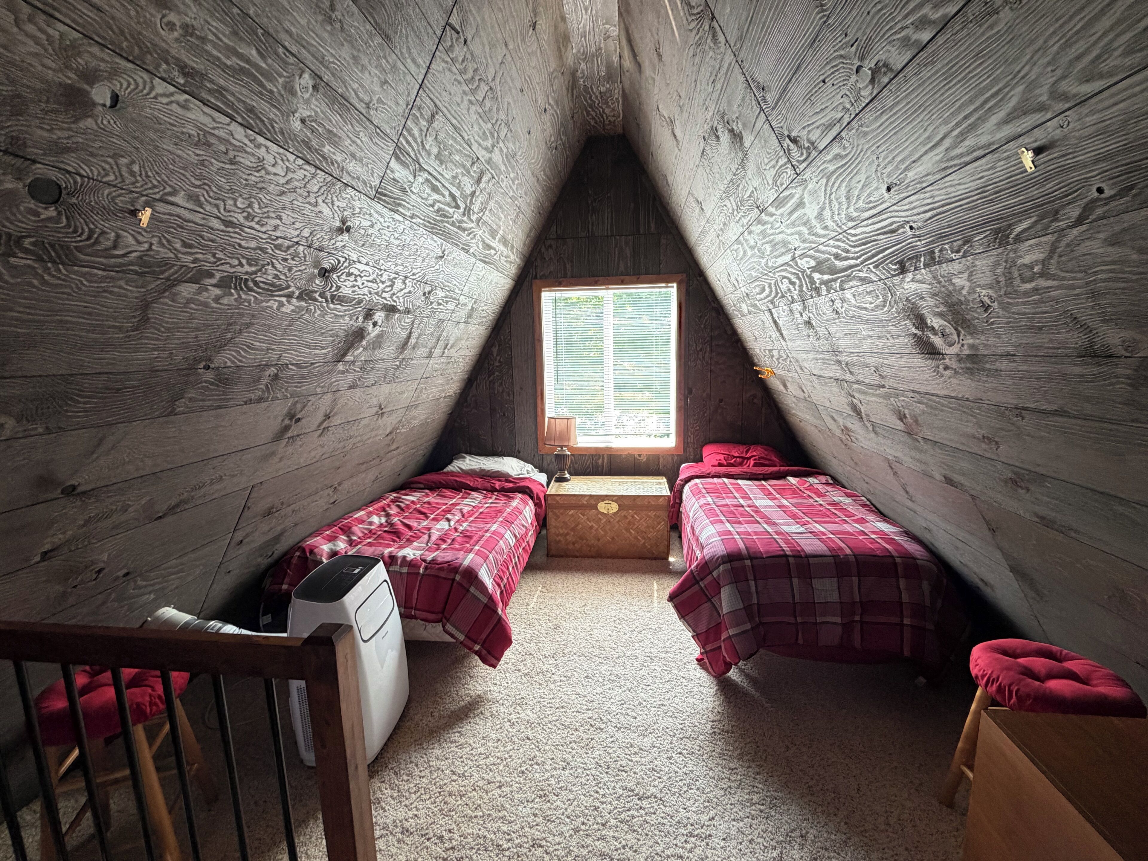 A small attic bedroom with two beds, a window, and a heater.