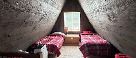 A small attic bedroom with two beds, a window, and a heater.