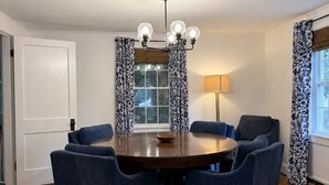 Un comedor con una mesa redonda, seis sillas, una araña y cortinas estampadas.