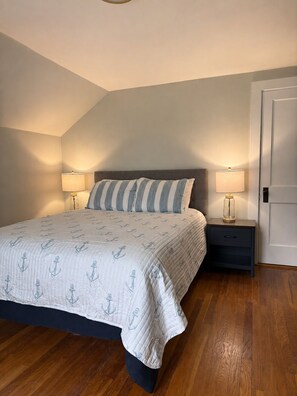 Une chambre à coucher avec un lit, deux tables de chevet avec des lampes, une porte et un plancher en bois.
