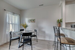 A dining area with a round table, four chairs, a vase with flowers, and a kitchen area with cabinets and a countertop. - The Cherry Nest 2-private suites townhome with a one-car garage (Nampa)