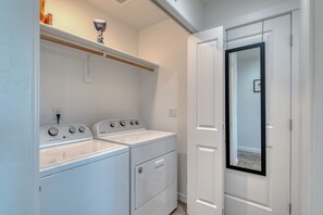 A laundry room with two front-loading washers and dryers, a shelf above the dryers, and a door leading to another room. - The Cherry Nest 2-private suites townhome with a one-car garage (Nampa)