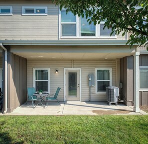 A residential building with a covered patio area, a small table with chairs, and an air conditioning unit. - The Cherry Nest 2-private suites townhome with a one-car garage (Nampa)