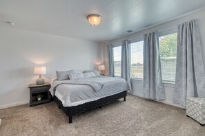 A bedroom with a bed, two bedside tables, a lamp, a window with curtains, and a ceiling light fixture. - The Cherry Nest 2-private suites townhome with a one-car garage (Nampa)