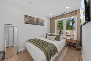 Un dormitorio con cama, mesita de noche, televisor y ventana con vistas.