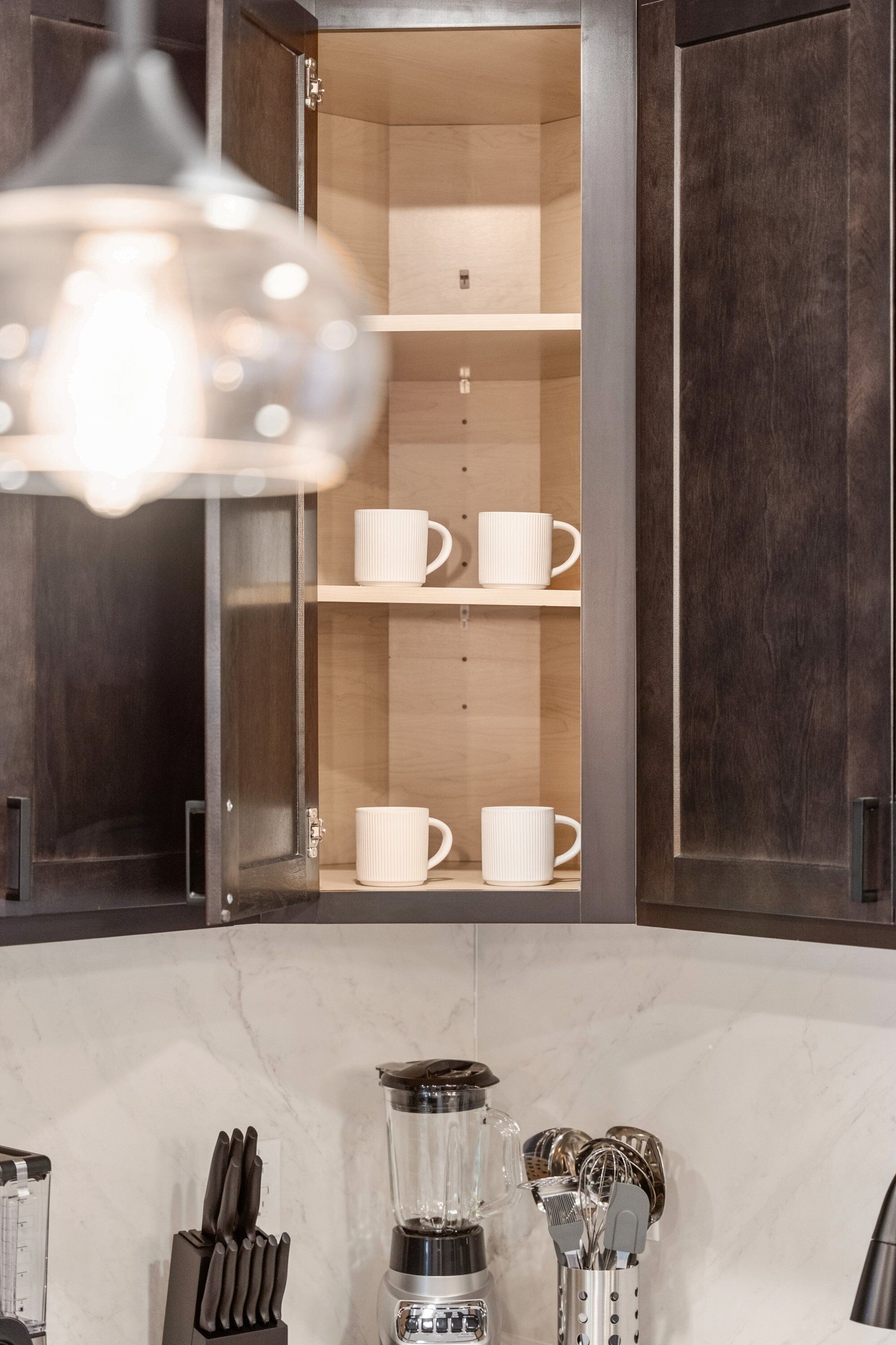A kitchen with a built-in cabinet containing white mugs, a coffee maker, and a knife block.
