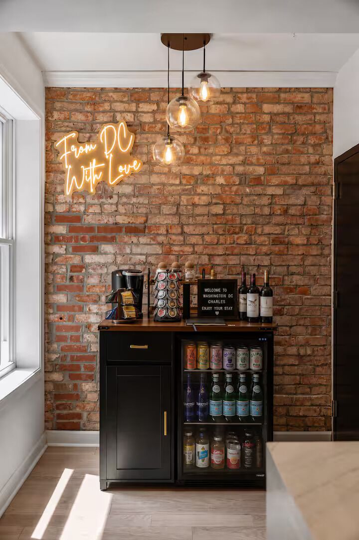 Ein Zimmer mit Backsteinwand, einer Neonreklame, einer Kaffeemaschine, einem Willkommensschild und einem Getränkespender.