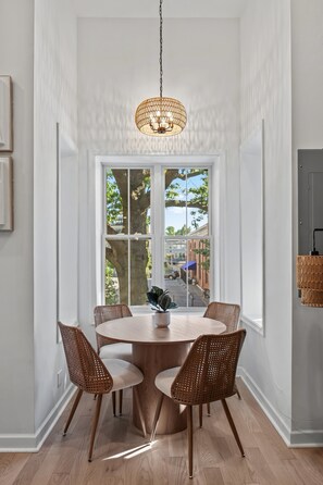En matplats med ett runt bord, fyra fåtöljer i rotting, en hängande lampa och ett stort fönster med utsikt över omgivningen.