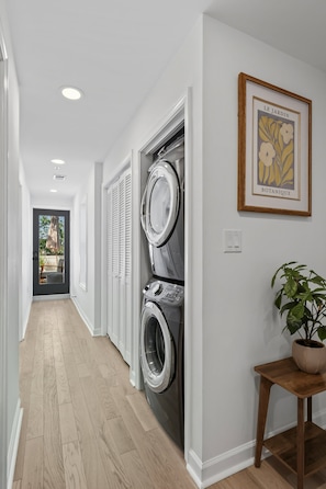 Ein Waschraum mit Waschmaschine und Trockner, einer hölzernen Bank und einem gerahmten Pflanzenmotiv an der Wand.