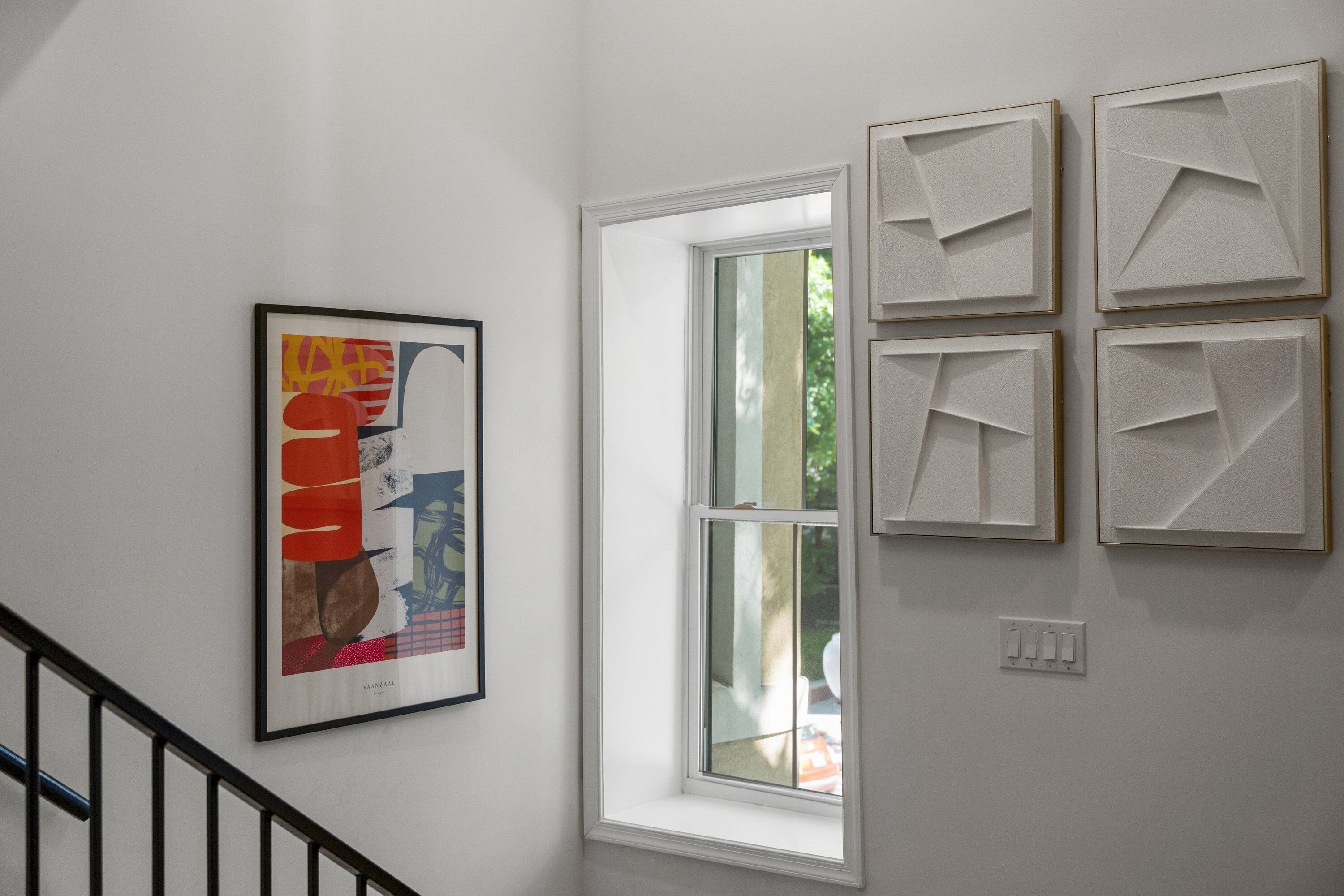 Eine Treppe mit Geländer, einem Fenster und einer Wand mit vier gerahmten Kunstwerken.