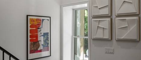 A staircase with a handrail, a window, and a wall with four framed artworks.
