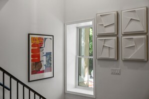 Una escalera con barandilla, una ventana y una pared con cuatro obras de arte enmarcadas.