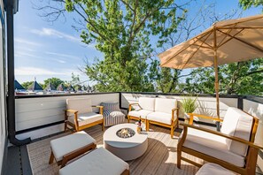 An outdoor seating area with a fire pit, cushioned seating, and a large umbrella. - Brand New 3BR Luxury DC Rowhome w/ Rooftop Patio• 5-10 mins from top attractions (Washington)