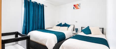 A hotel room with two beds, a crib, a chandelier, and a painting on the wall.