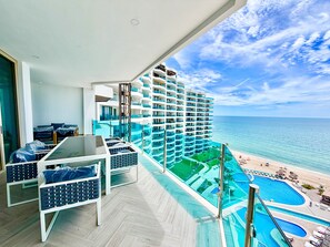 Et højt hotel med balkon, udsigt over pool og strand.