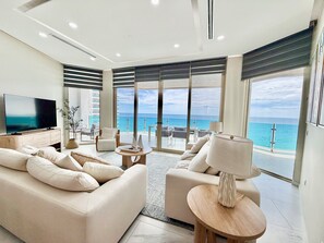 Ein modernes Wohnzimmer mit einem großen Flachbildfernseher, bequemen Sitzmöglichkeiten und Meerblick durch große Fenster.