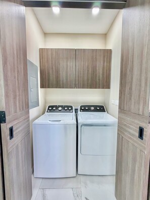 A laundry room with two white front-loading washing machines, wooden cabinets above, and a tiled floor. - Esmeralda Beach Resort 3 Bedrooms Condo D 902 (Puerto Peñasco)