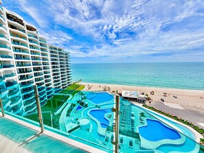 Ein Hotel mit mehreren Etagen, einem großen Schwimmbecken mit verschiedenen Bereichen und Blick auf den Strand.